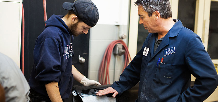 An instructor and gloved student work on refinishing a body panel